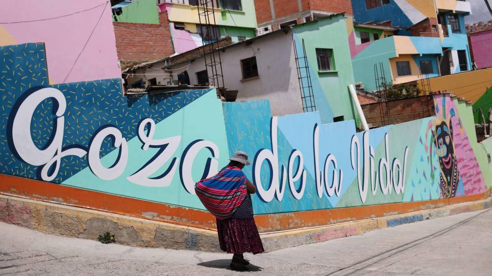 Fotografía del 26 de noviembre de 2024 de una mujer junto a un mural en el barrio de Chualluma, en La Paz (Bolivia).