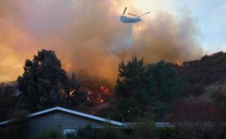 Un helicóptero arroja agua sobre una casa durante el incendio forestal de Palisades en Los Ángeles, California.