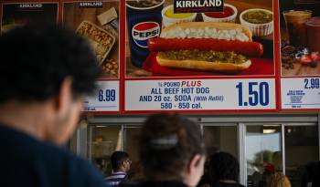 Los clientes esperan en fila para ordenar debajo de los carteles del combo Costco Kirkland Signature de hot dog y refresco de $1.50.