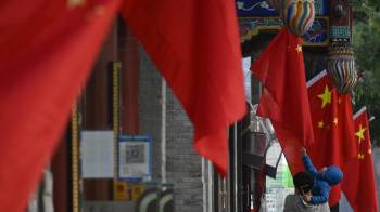 Un niño toca una bandera china colgada en una calle de Beijing, en China.