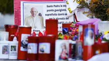 Los fieles dejan velas y tarjetas a los pies de la estatua de Juan Pablo II en la entrada del Hospital Gemelli, donde está hospitalizado el Papa Francisco.