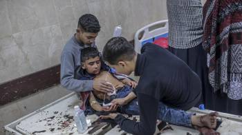 Dos niños ayudan a su hermano pequeño herido en el hospital Al Aqsa tras un ataque aéreo israelí en el campo de refugiados de Al Bureije, en el centro de Gaza.