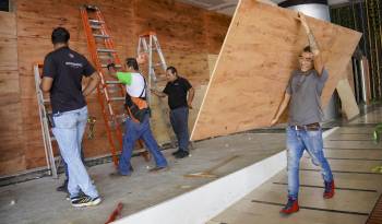 Trabajadores colocan láminas de madera sobre ventanas y puertas de vidrio para protegerlas de los fuertes vientos que se esperan con la llegada del huracán Milton a la zona hotelera de Cancún.