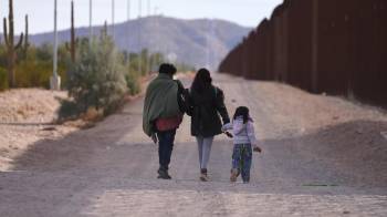 Una familia camina a lo largo del muro fronterizo de Estados Unidos buscando a la Patrulla Fronteriza estadounidense para entregarse para su procesamiento en Lukeville, Arizona.