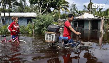 Dos personas caminan con bicicletas por una calle inundada de agua del mar este jueves, tras el paso del huracán Helen, en el poblado de Guanimar, en la costa sur de la provincia de Artemisa, Cuba.