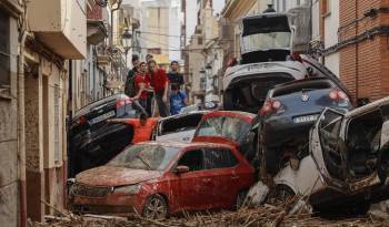 Vecinos de Paiporta intentan pasar entre una montonera de vehículos arrastrados por la corriente, este viernes.