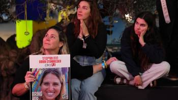 Varias personas observan una transmisión en vivo en una pantalla grande que informa sobre la liberación de tres rehenes israelíes, Romi Gonen, Emily Damari y Doron Steinbrecher, transferidos de Hamás a la Cruz Roja.