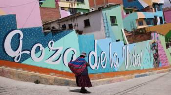 Fotografía del 26 de noviembre de 2024 de una mujer junto a un mural en el barrio de Chualluma, en La Paz (Bolivia).