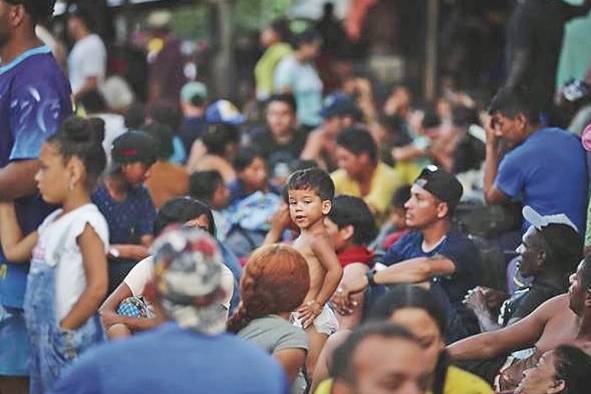 Migrantes hacen fila para dar sus datos personales a agentes de migración.