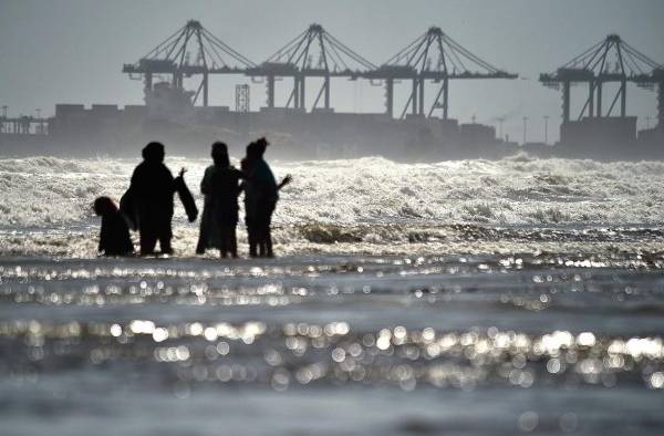 Imagen donde se observan personas frente al mar donde se muestra al fondo un área portuaria y la actividad de las olas.