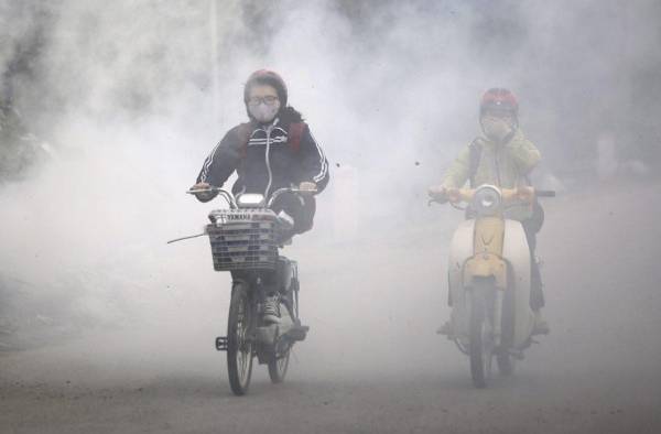 En la imagen de archivo, varias personas circulan entre el humo generado por residuos quemados en las calles de Hanoi, Vietnam.