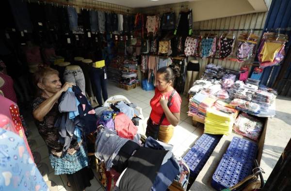 Una mujer muestra prendas de vestir a una clienta en una tienda de ropa, el 18 de abril de 2023, en el centro de San Salvador