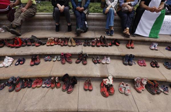 Un grupo de personas junto a zapatos teñidos de rojo, se manifiestan hoy, frente al palacio de La Moneda, en Santiago de Chile.