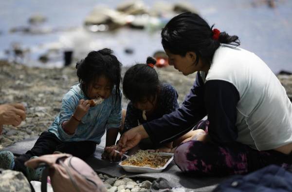 Una migrante ecuatoriana come junto a sus hijas en la selva mientras esperan para ser trasladados en canoa en Bajo Chiquito, Darién