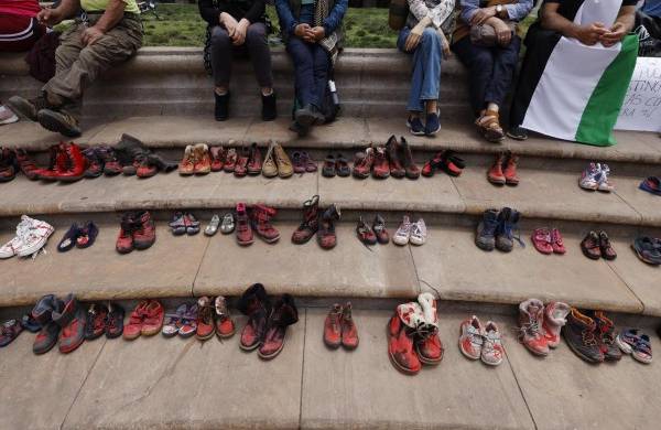 Un grupo de personas junto a zapatos teñidos de rojo, se manifiestan hoy, frente al palacio de La Moneda, en Santiago de Chile.