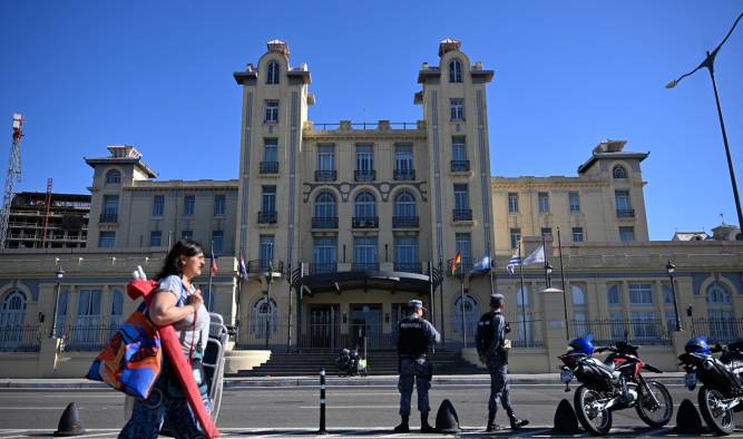 Una mujer pasa mientras oficiales de la Armada de Uruguay hacen guardia frente al Palacio del Mercosur antes de la sesión inaugural de la LXV Cumbre del Mercosur en Montevideo.