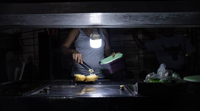 Una persona vende comida ayudado con un bombillo en medio de la oscuridad durante un corte eléctrico, el 29 de febrero de 2024 en Maracaibo (Venezuela).