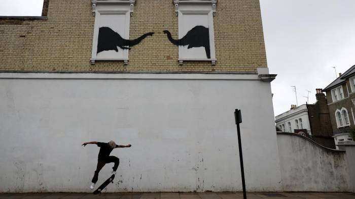 Un hombre en una patineta bajo la nueva obra del artista callejero británico, Banksy.