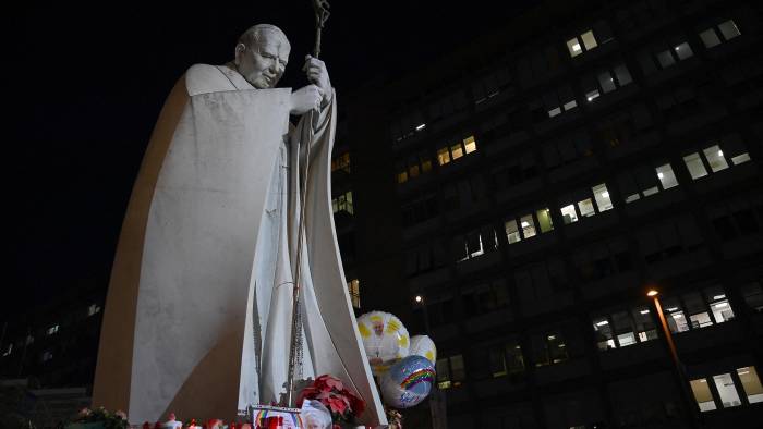 Globos están atados a la estatua de Juan Pablo II, donde las personas llevan velas y acuden a rezar afuera del hospital Gemelli, en Roma, donde el papa Francisco está hospitalizado.