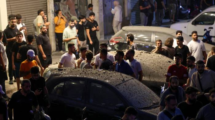 Los transeúntes rodean vehículos cubiertos de escombros cerca del lugar de un ataque militar israelí en los suburbios del sur de Beirut el 30 de julio de 2024.