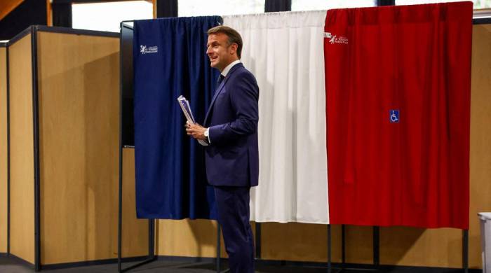 France's President Emmanuel Macron stands in front of a polling booth, adorned with curtains displaying the colors of the flag of France, before casting his ballot for the European Parliament election at a polling station in Le Touquet, northern France on June 9, 2024.