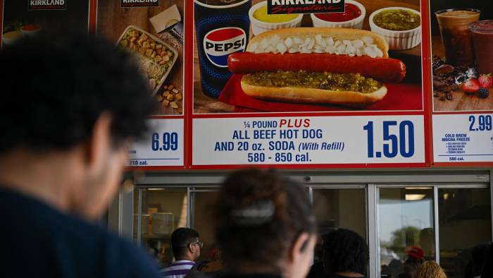 Los clientes esperan en fila para ordenar debajo de los carteles del combo Costco Kirkland Signature de hot dog y refresco de $1.50.