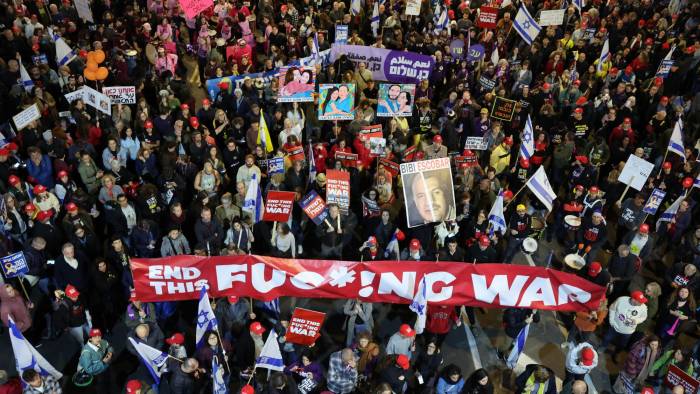 La gente sostiene carteles y ondea banderas durante una protesta antigubernamental que pide acciones para asegurar la liberación de los rehenes israelíes que se encuentran cautivos desde los ataques del 7 de octubre de 2023.