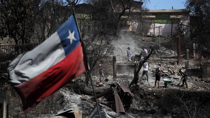 Una bandera chilena ondea mientras los vecinos limpian sus tierras y queman casas en Villa Independencia, región de Valparaíso, Chile.