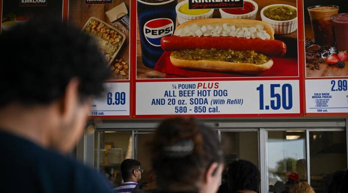 Los clientes esperan en fila para ordenar debajo de los carteles del combo Costco Kirkland Signature de hot dog y refresco de $1.50.