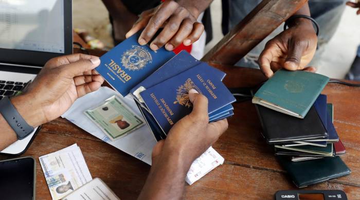 Fotografía de archivo de una persona mientras recibe pasaportes de migrantes de diversas partes del mundo que compran tiquetes para Capurganá, en el embarcadero de Necoclí (Colombia).