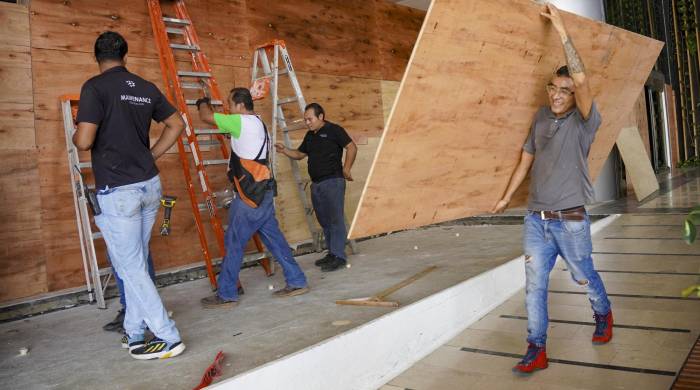 Trabajadores colocan láminas de madera sobre ventanas y puertas de vidrio para protegerlas de los fuertes vientos que se esperan con la llegada del huracán Milton a la zona hotelera de Cancún.