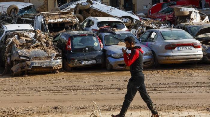 Un hombre camina junto a los coches apilados en Catarroja, Valencia este martes, una de las localidades más afectados por las inundaciones.