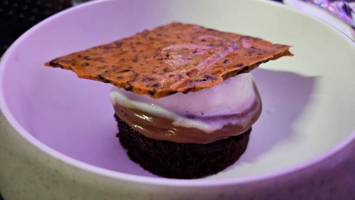 ‘Cake’ de chocolate con sirope de café, maracuyá y ganache de chocolate, decorado con brittle de cacao nibs y servido con un quenelle de helado de vainilla.