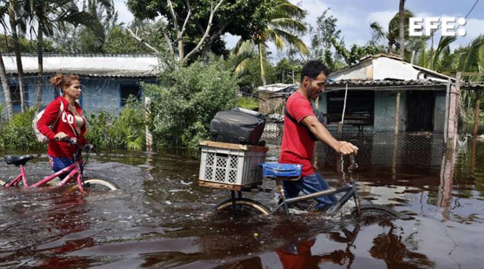 Dos personas caminan con bicicletas por una calle inundada de agua del mar este jueves, tras el paso del huracán Helen, en el poblado de Guanimar, en la costa sur de la provincia de Artemisa, Cuba.