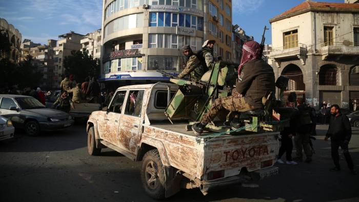 Rebeldes sirios en la parte trasera de un vehículo mientras la gente celebra en las calles de Homs, Siria.