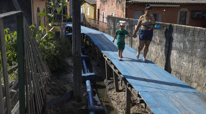 Personas caminan junto a un sistema de alcantarillado el 11 de junio de 2024 en una zona de la ciudad de Manaos, capital del estado de Amazonas (Brasil).