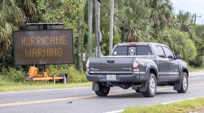 Un vehículo avanza junto a una señal de 'evacuación obligatoria y advertencia de huracán'.