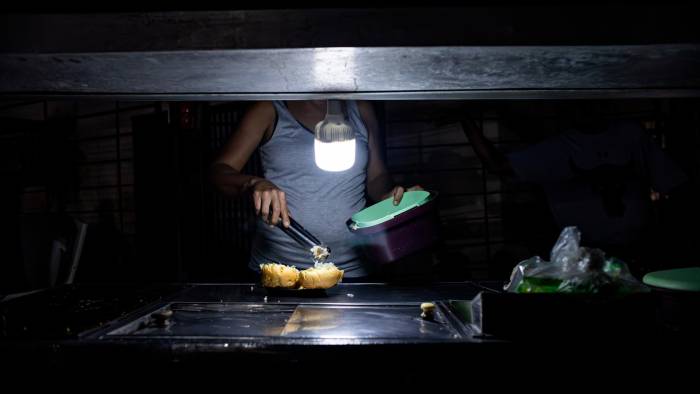 Una persona vende comida ayudada con un bombillo en medio de la oscuridad durante un corte eléctrico, el 29 de febrero de 2024 en Maracaibo, Venezuela.