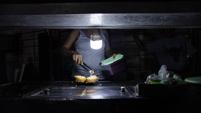 Una persona vende comida ayudada con un bombillo en medio de la oscuridad, durante un corte eléctrico, el 29 de febrero de 2024 en Maracaibo (Venezuela).