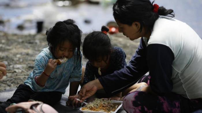 Una migrante ecuatoriana come junto a sus hijas en la selva mientras esperan para ser trasladados en canoa desde la Quebrada León hasta a la comunidad de Bajo Chiquito en Darién.